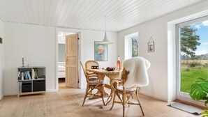 Una habitación luminosa con piso de madera, una mesa de comedor con sillas, una estantería y un ventanal con vistas a zonas verdes.