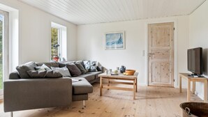 Una sala de estar moderna con un sofá seccional gris, una mesa de centro de madera, un televisor sobre un mueble de madera y una puerta con acabado rústico.
