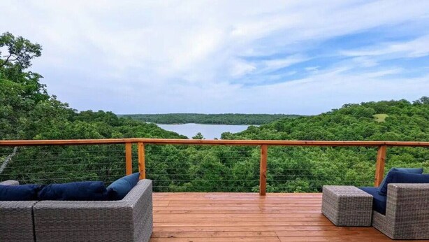 A wooden deck with wicker furniture and a railing overlooking a lake surrounded by trees. - Lakeview Hideaway - Amazing View of Lake of the Arbuckles (Sulphur)