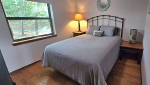 A bedroom with a bed, a bedside table, a lamp, a window, and a wall decoration. - Lakeview Hideaway - Amazing View of Lake of the Arbuckles (Sulphur)