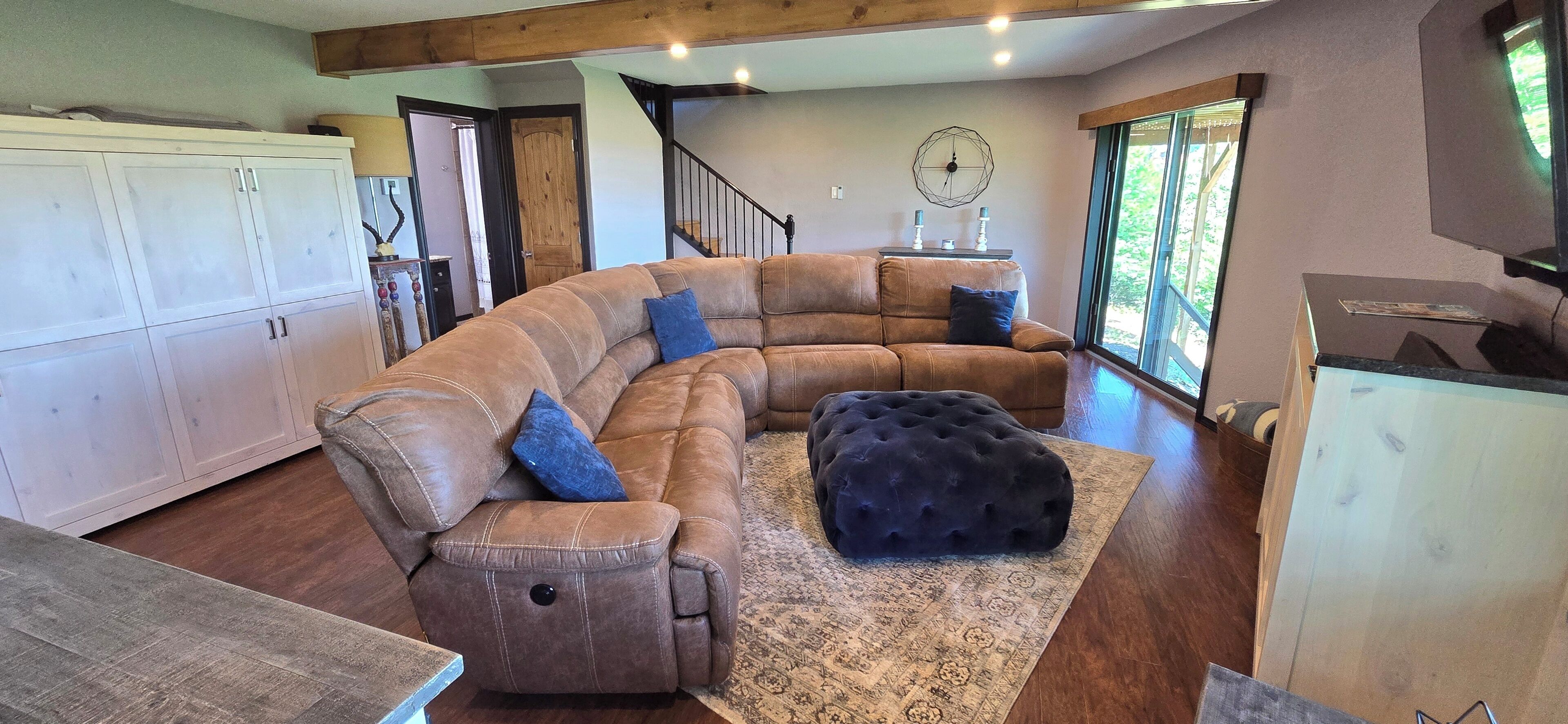 A spacious living room with a large L-shaped sectional sofa, a dark ottoman, and a patterned rug.