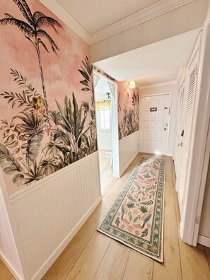 Un couloir orné d’une fresque florale, doté d’un plancher en bois et d’une porte avec une plaque numérotée.