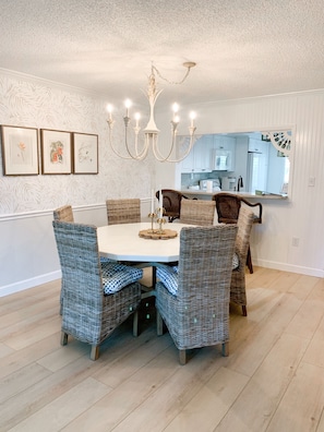 A dining area with a round table, wicker chairs, a chandelier, and framed botanical prints on the wall.