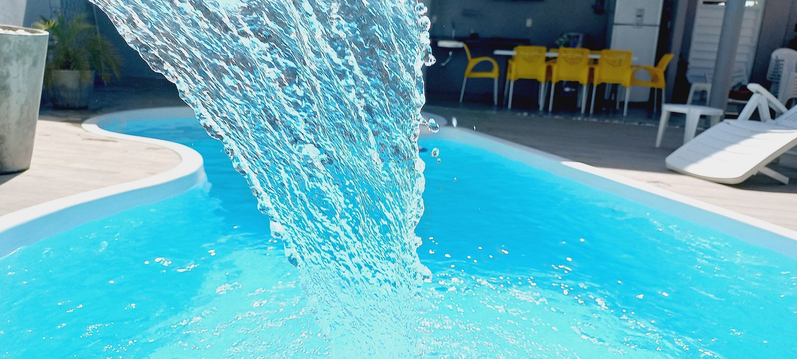 A swimming pool with a water feature, surrounded by lounge chairs and yellow tables.
