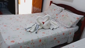 A neatly made bed with floral bedding, a wooden headboard, and a pair of towels arranged in a swan shape. - Casa Paraíso das Conchas (Barra de São Miguel)