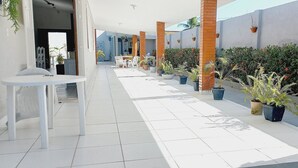 A clean, modern outdoor area with a tiled floor, a white table, and potted plants. - Casa Paraíso das Conchas (Barra de São Miguel)