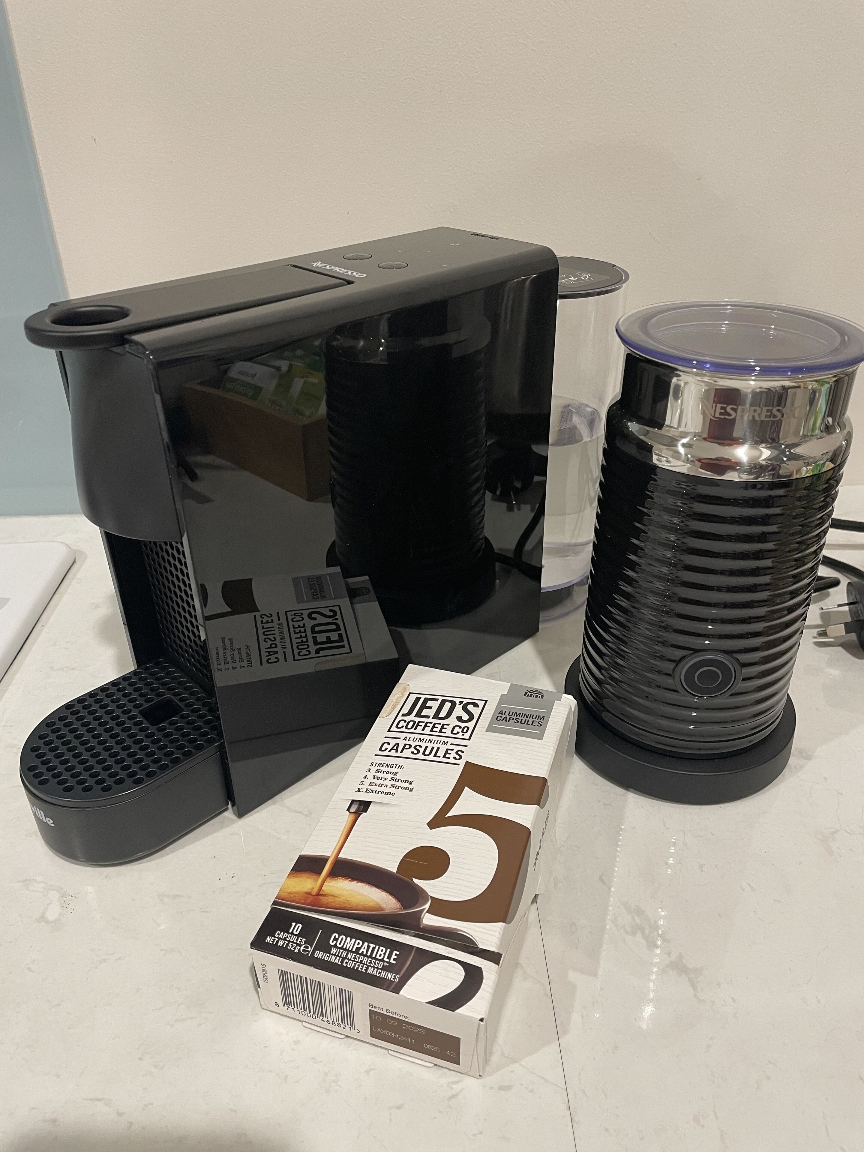 Una cafetera, una caja de cápsulas de café JED y una máquina de café Nespresso sobre una encimera.