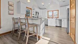 A modern kitchen with white cabinets, a central island, wooden chairs, and pendant lighting. - 7 Ensuites + Private Pool + 5 Min Walk to Downtown (Kitty Hawk)