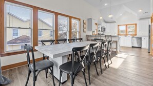 A spacious kitchen with white cabinets, a large island, and a dining area with a long table and chairs. - 7 Ensuites + Private Pool + 5 Min Walk to Downtown (Kitty Hawk)