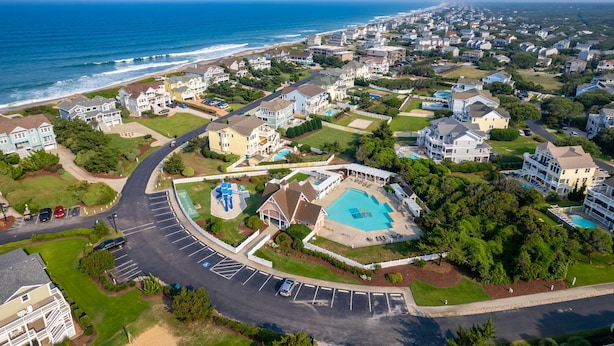 An aerial view of a coastal residential area with houses, a swimming pool, and a road. - 7 Ensuites + Private Pool + 5 Min Walk to Downtown (Kitty Hawk)