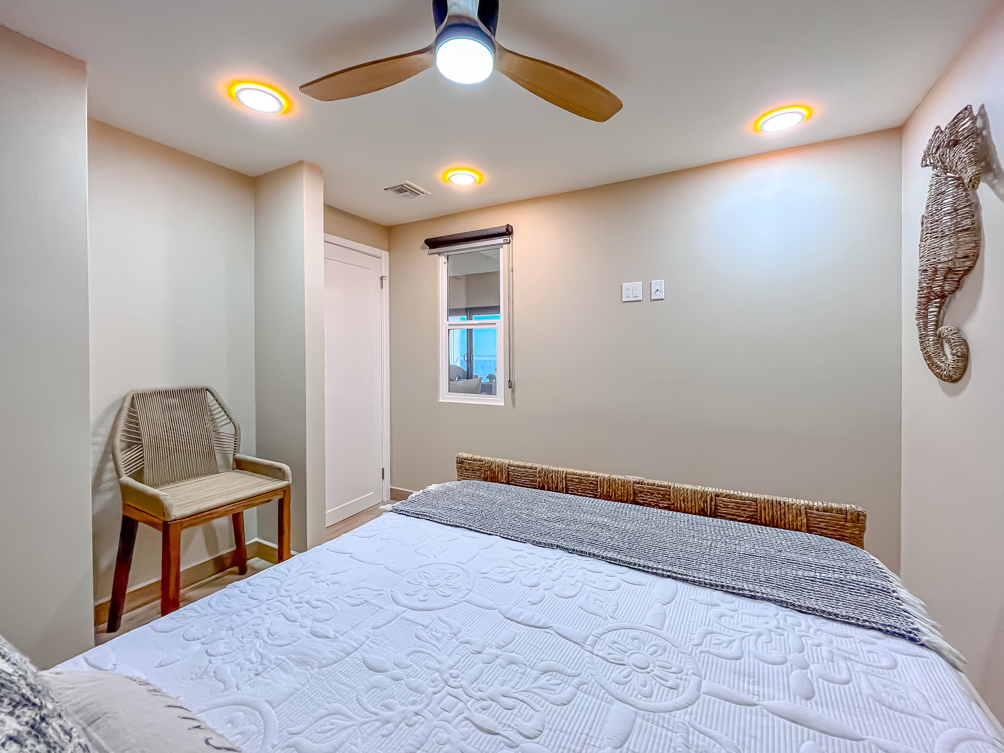 A bedroom with a large bed, a chair, a ceiling fan, and a window with a view.