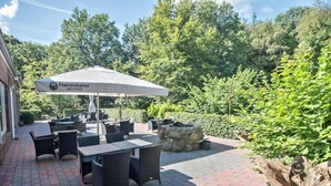 An outdoor patio area with tables and chairs, a stone fire pit, and a large umbrella.