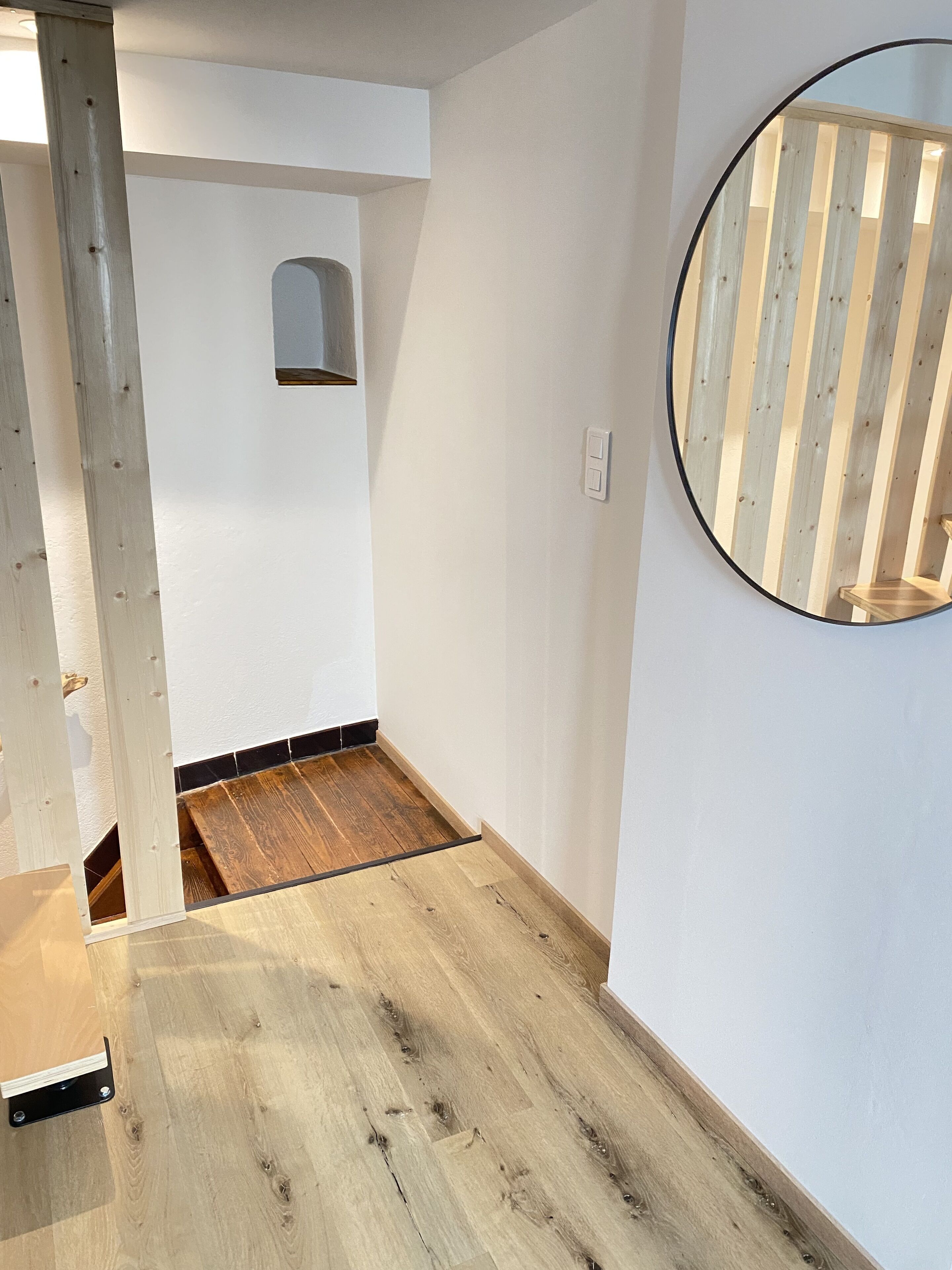 Een kamer met een houten vloer, witte muren en een ronde spiegel met houten lijst.