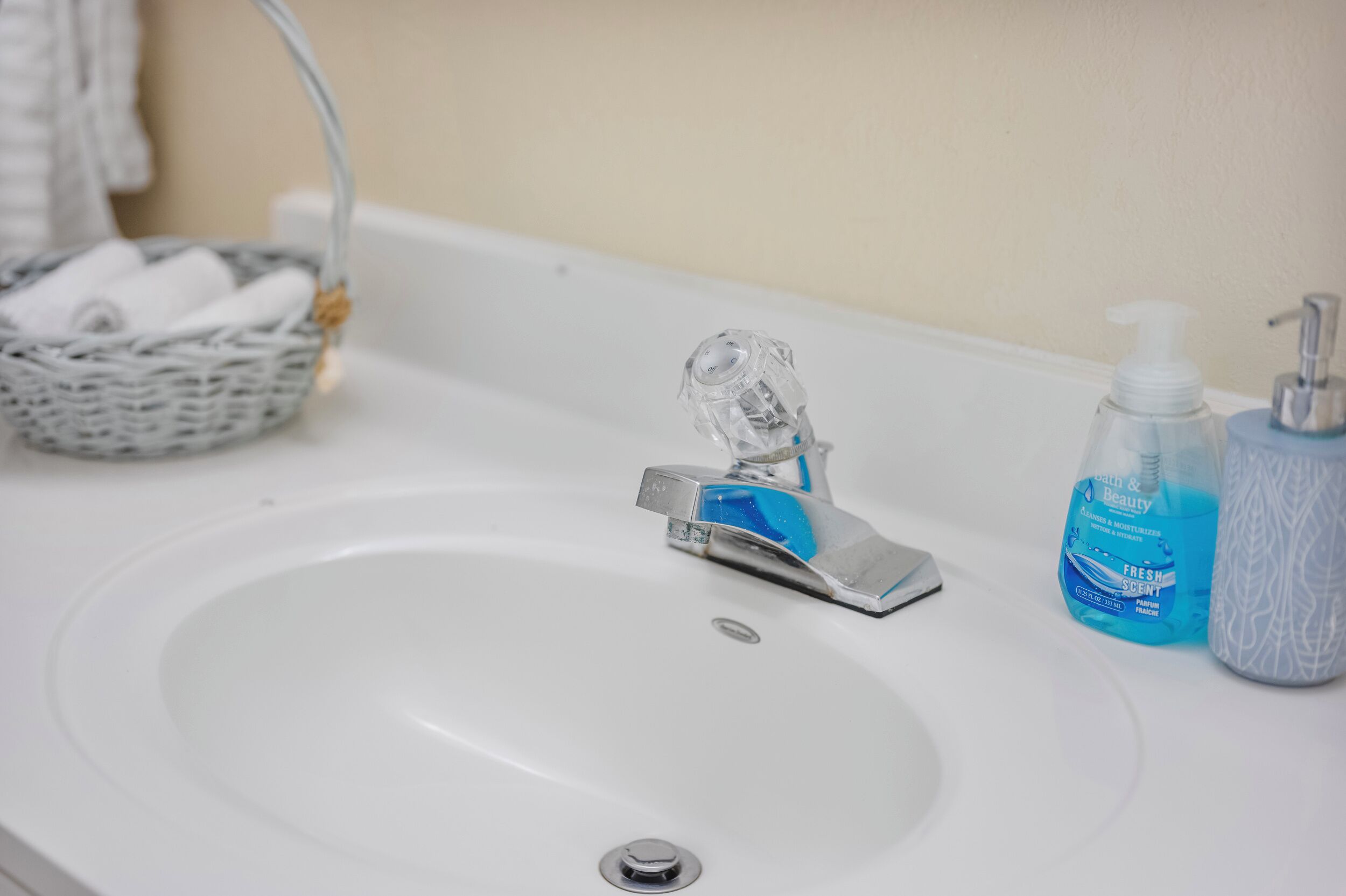 A bathroom sink with a chrome faucet, a blue soap dispenser, and a white bottle of hand soap.