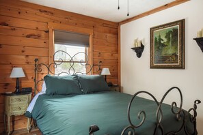 A wooden-paneled room with a bed, a nightstand with a lamp, and a wall-mounted shelf with candles. - New Hot Tub - Sweet Pines Cabin - Sleeps up to 8 (Patriot)