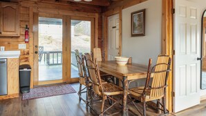 A wooden interior with a dining table, chairs, a fire extinguisher, and a door leading outside. - New Hot Tub - Sweet Pines Cabin - Sleeps up to 8 (Patriot)
