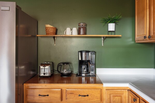 A kitchen with a wooden countertop, a coffee maker, a toaster, and a shelf with cups and a basket. - New Hot Tub - Sweet Pines Cabin - Sleeps up to 8 (Patriot)