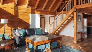A spacious living area with a wooden ceiling, a staircase, and a sofa with cushions. - New Hot Tub - Sweet Pines Cabin - Sleeps up to 8 (Patriot)