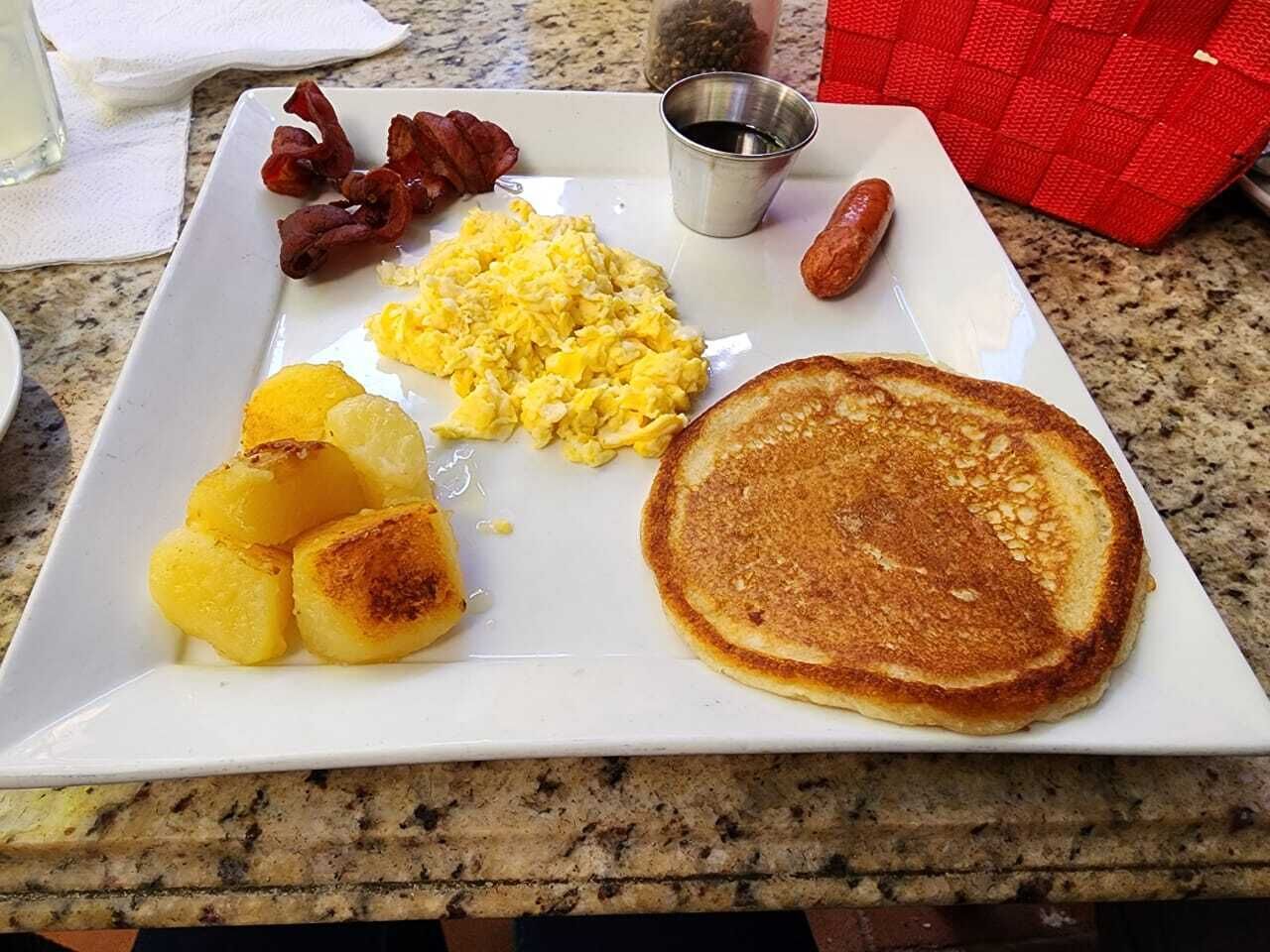 A breakfast plate with scrambled eggs, bacon, sausage, toast, and potatoes.