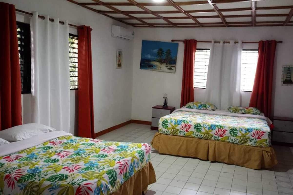 Ein Zimmer mit zwei Betten, roten Vorhängen, einem Gemälde und einem Fliesenboden.