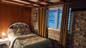 A cozy bedroom with a wooden ceiling, a bed with a headboard, a window with curtains, and a stone-patterned wall. - BOCA DEL PARAISO (Boca Chica)
