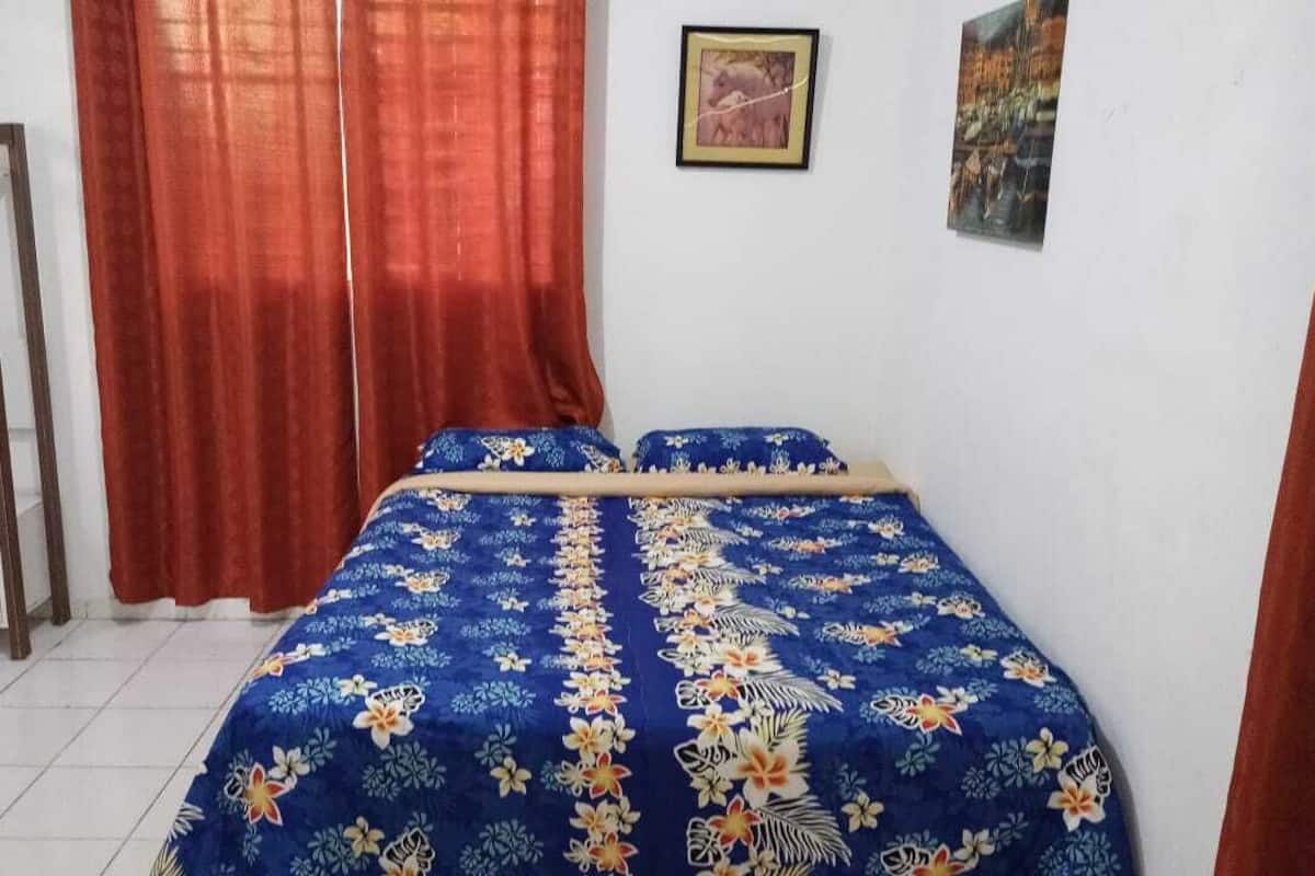 Ein Schlafzimmer mit Bett, Vorhängen, einem kleinen Tisch und Wandbildern.