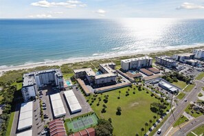 An aerial view of a coastal hotel complex with multiple buildings, a beach, and a tennis court.