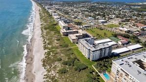 Vista aèria d'una zona costanera amb un hotel a primera línia de mar, amb diversos edificis, una piscina i una carretera que discorre paral·lela a la platja.