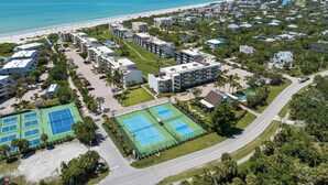 Luchtbeeld van een kustresort met meerdere gebouwen, een strand en tennisterreinen.