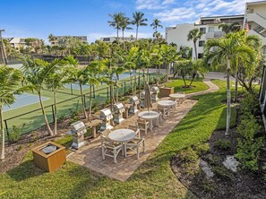 Een terras buiten met barbecuegrills, zitplaatsen en een tennisbaan.