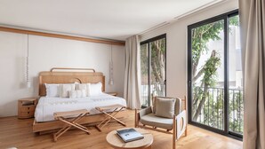 Une chambre d’hôtel moderne avec un grand lit, un plancher en bois, une table basse ronde, une chaise et une vue sur l’extérieur grâce à une grande fenêtre.