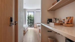 Une chambre d’hôtel moderne avec un plancher en bois, un lit, un bureau et un balcon donnant sur un paysage verdoyant.