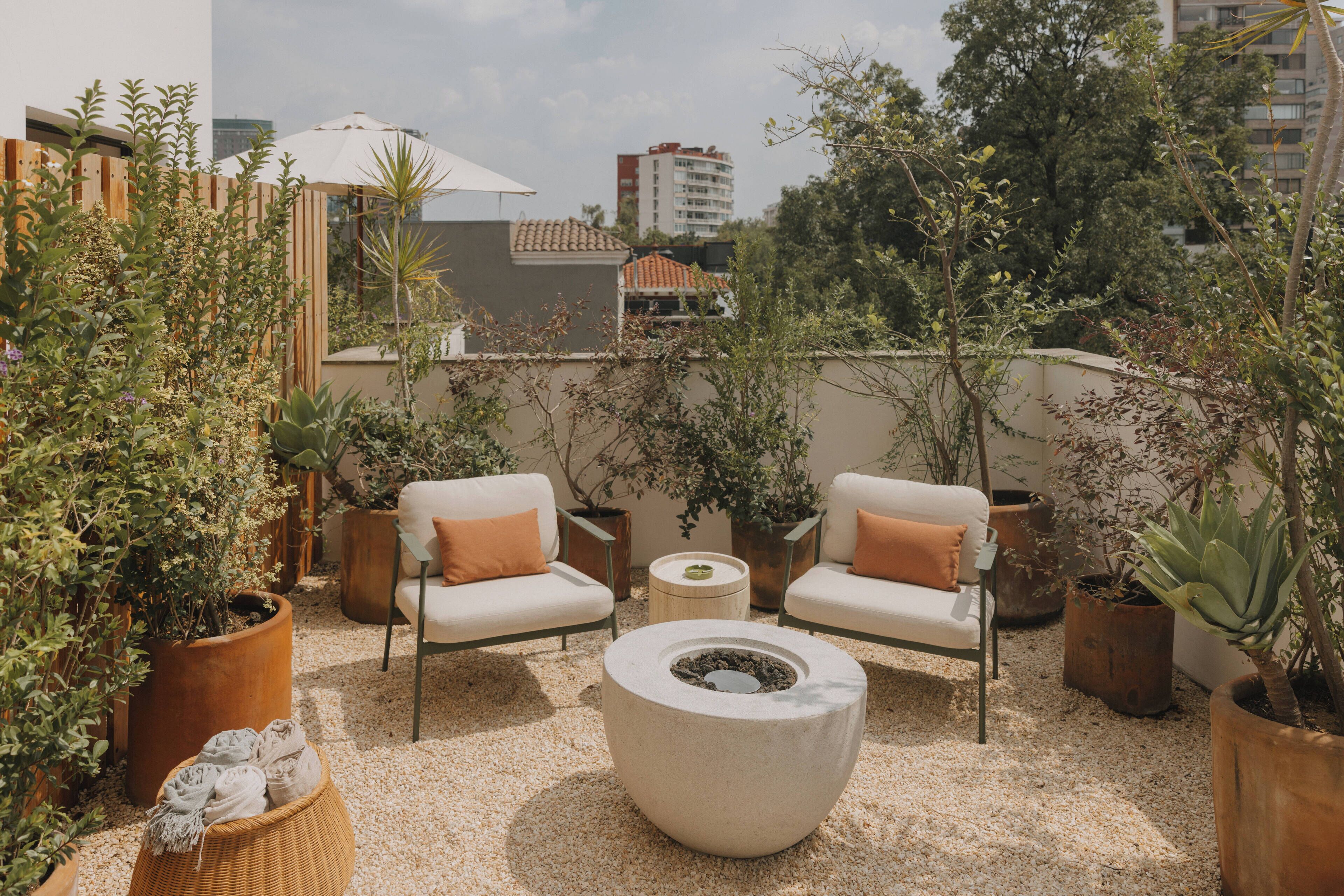 Um terraço no telhado com dois sofás brancos, uma mesa redonda e plantas em vasos.