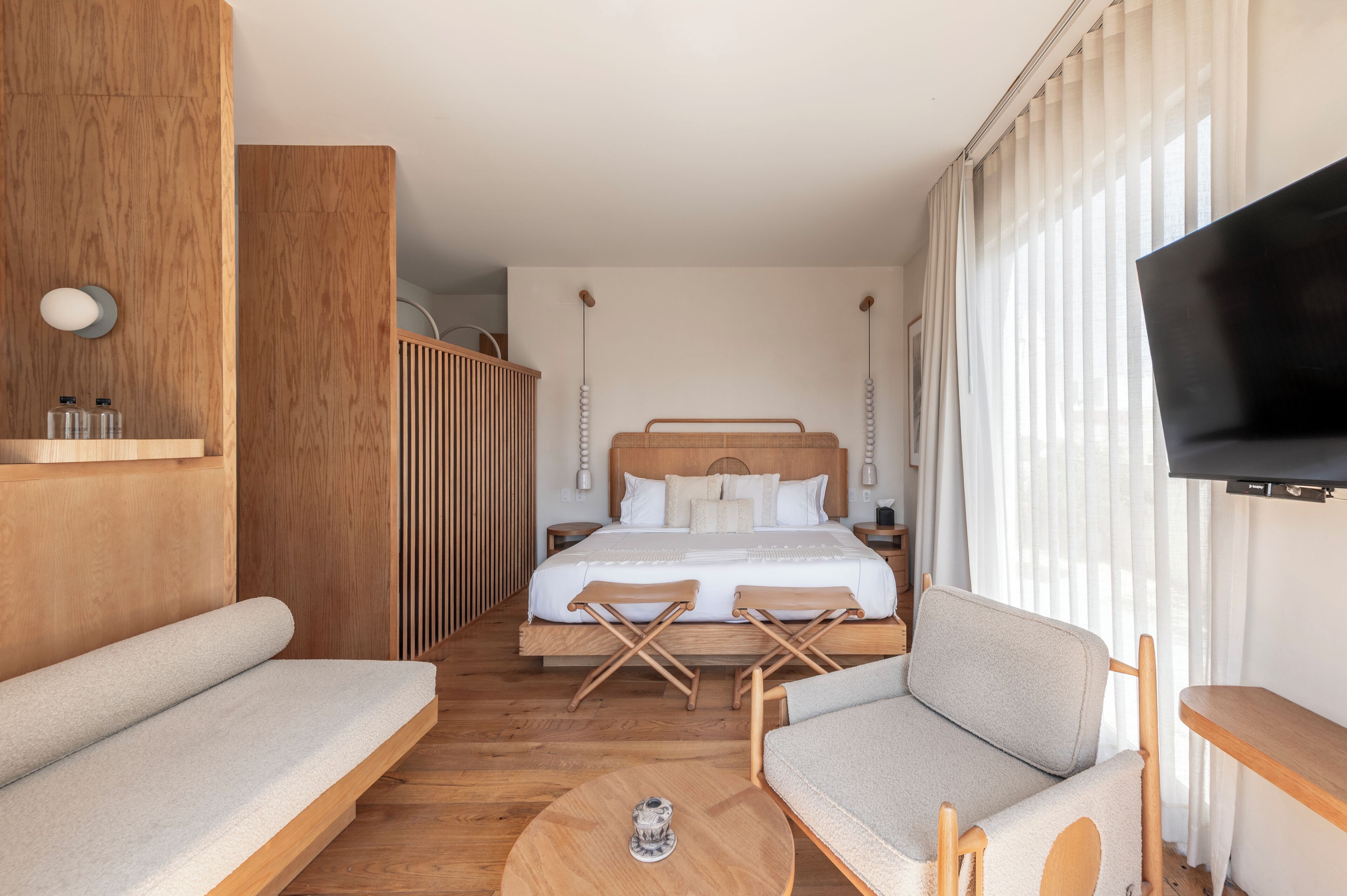 A modern hotel room with a large bed, a TV, a sofa, and a small table.