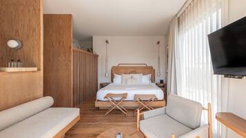 A modern hotel room with a large bed, a TV, a sofa, and a small table.