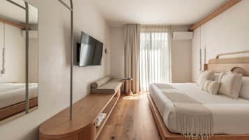 A modern bedroom with a wooden floor, a large bed with white bedding, a TV mounted on the wall, and a bedside table with a lamp.