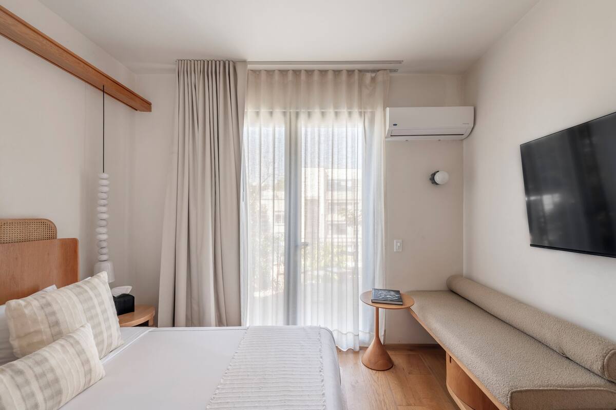 Moderni hotellihuone, jossa on sänky, penkki, televisio ja ilmastointilaite.