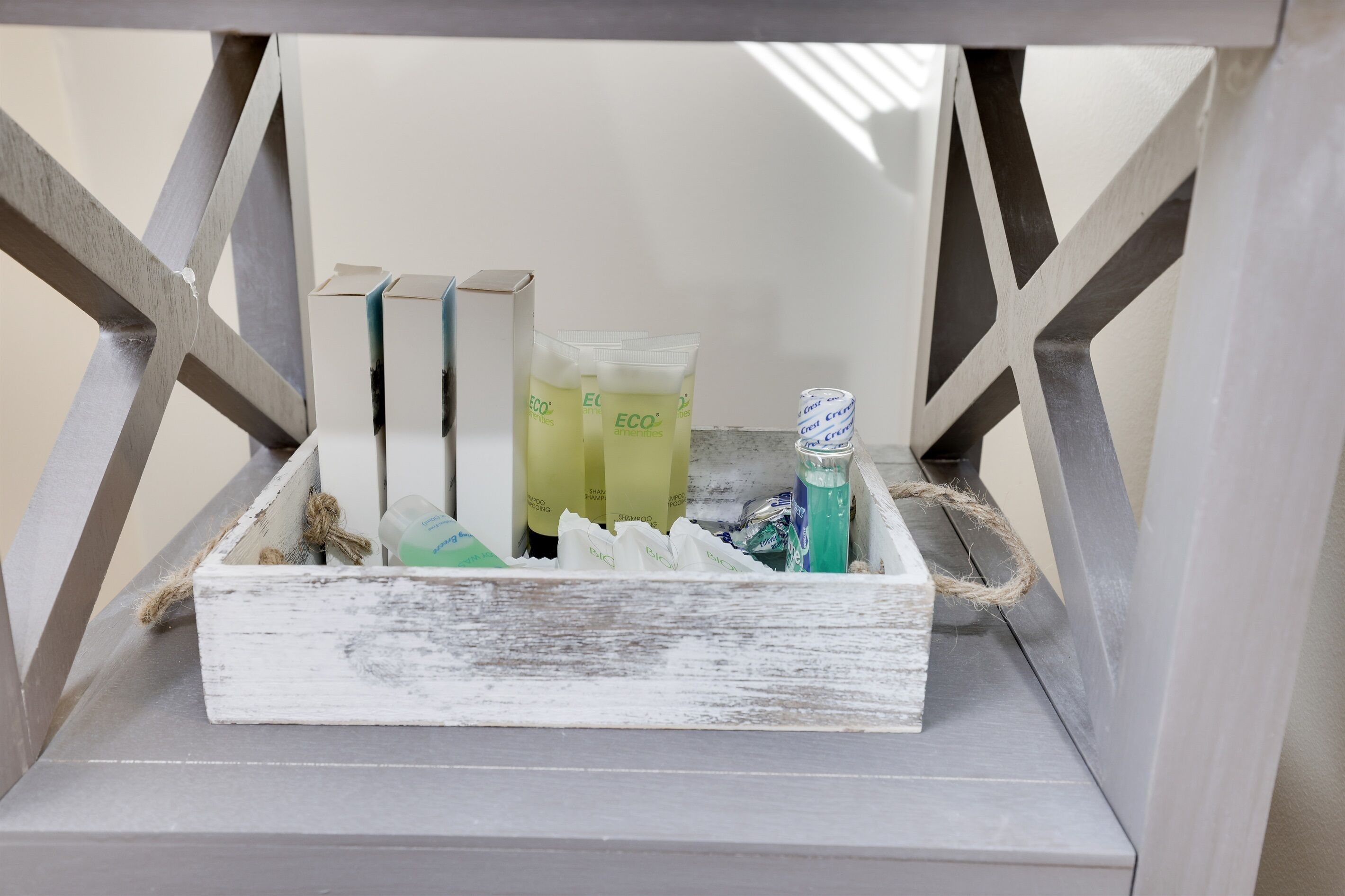 A rustic wooden crate with various toiletries, including bottles and tubes, placed on a shelf with a simple geometric design.
