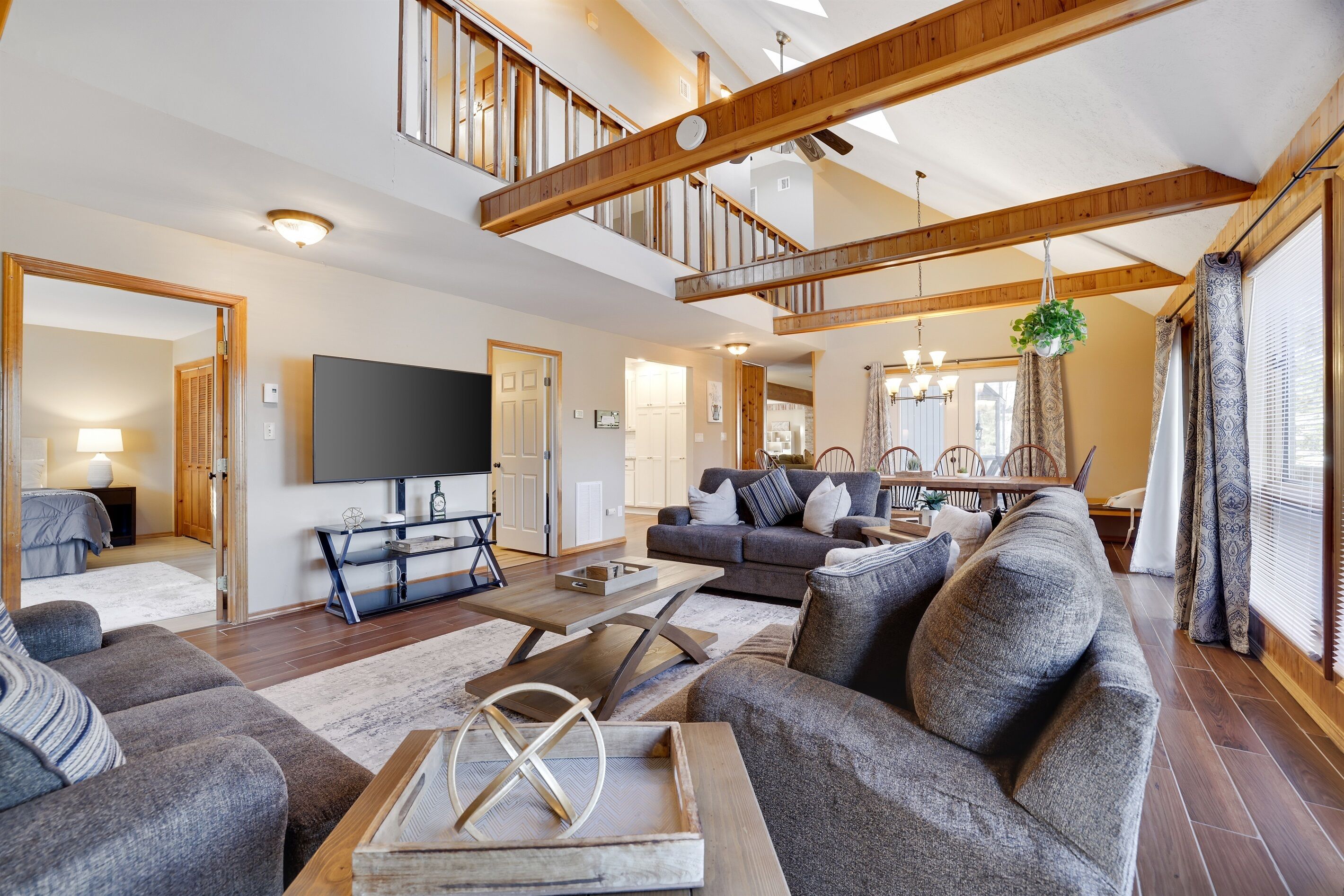 A spacious living room with a large sofa set, a coffee table, and a flat-screen TV mounted on the wall.