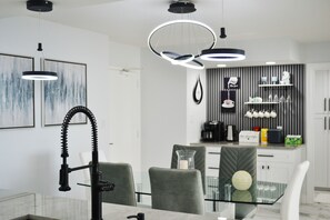 Un comedor moderno con una mesa de vidrio, sillas tapizadas en gris e iluminación colgante.