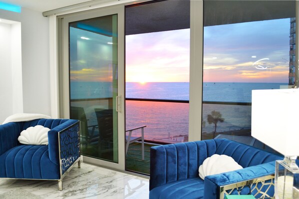 Una habitación con dos sofás azules, una lámpara blanca y vistas al océano al atardecer.