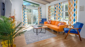 A modern living room with a wooden ceiling, a sofa, a chair, a coffee table, and a large window with patterned curtains. - Retro River House! Waterfront, Firepit, BBQ, Gameroom, 1 min to Sequoia Park.  (Three Rivers)