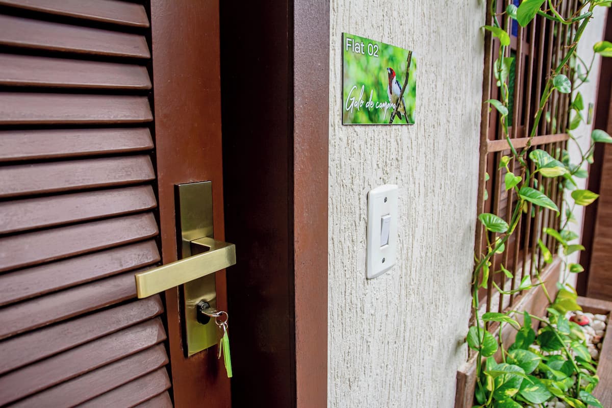 A wooden door with horizontal slats, a brass handle, and a keyhole. A green sign with "Flat 02" and "Gobo de camping" is visible.