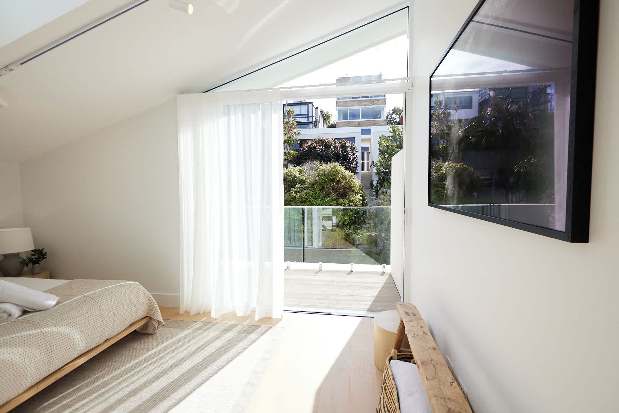 Quarto com cama, mesa de cabeceira, TV fixada na parede e varanda com porta de vidro.