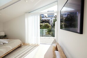 Un dormitorio con cama, mesita de noche, televisor montado en la pared y balcón con puerta de vidrio.