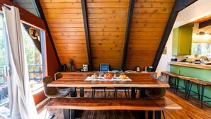Een houten eettafel met banken, een keuken met groene kastjes, en uitzicht op het omliggende landschap door een raam.