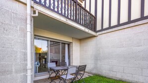 Un patio con tavolo e sedie, una porta vetrata che dà su un balcone e una zona verde.