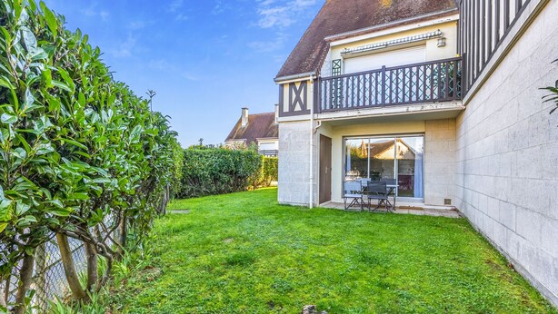 Un immobile residenziale con un prato curato, una zona pranzo con arredi da esterno e un balcone con ringhiera.