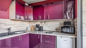 Una cucina compatta con mobili viola, una macchina da caffè, un tostapane ed una lavastoviglie.