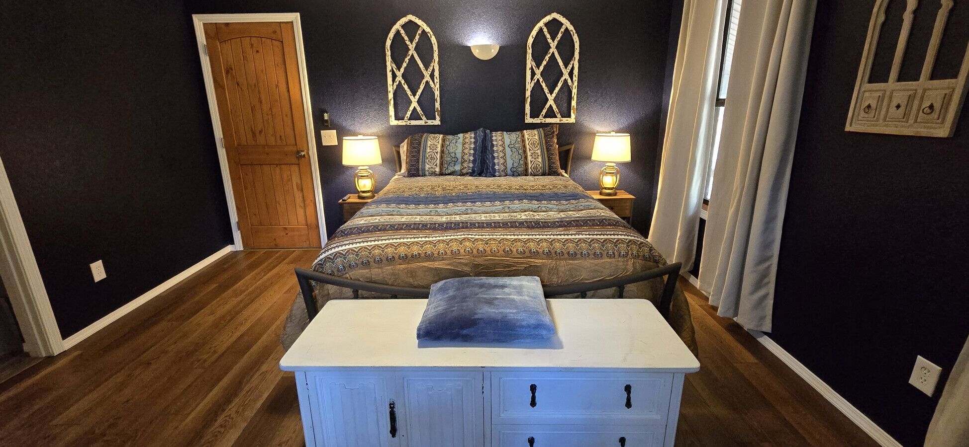 A bedroom with a bed, bedside lamps, a wooden door, and a nightstand.